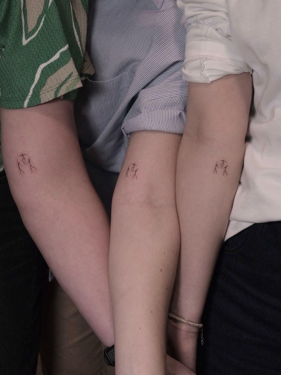 Three friends side by side showing the same small tattoo on their forearms