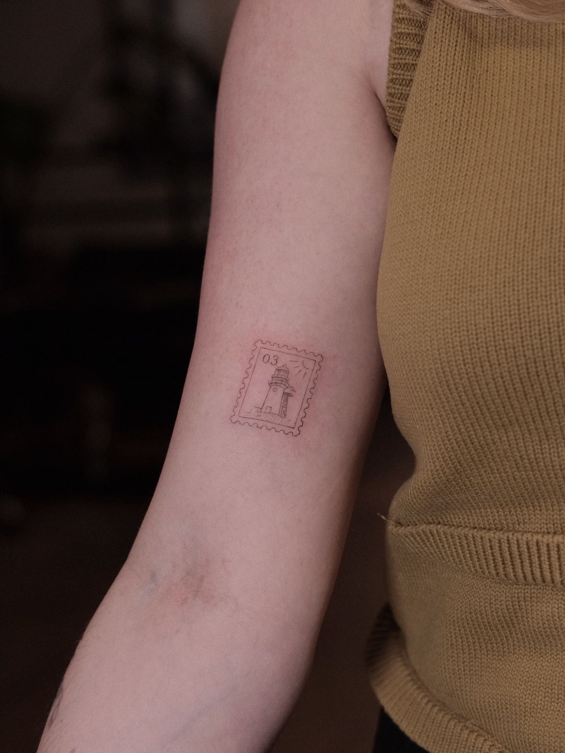 Postage stamp tattoo in red ink on the arm